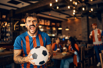 Passionate soccer fan shouting while watching game in bar.