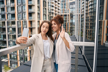 Two elegant office workers taking selfie outdoors