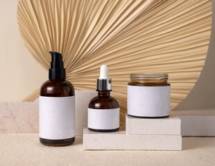 Glass bottles on travertine stone against dry palm leaf  on beige close up, cosmetic mockup