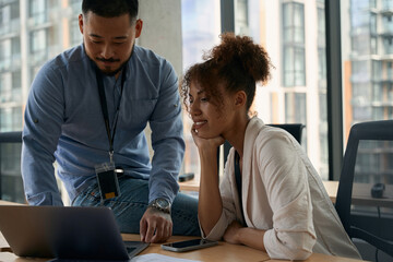 Corporate worker working on laptop guided by his colleague