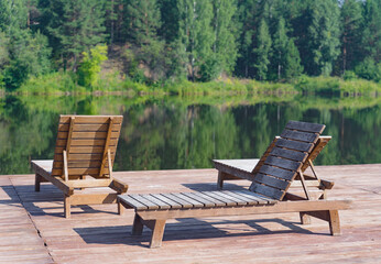 The hotel's terrace with wooden sun loungers is located on the shore of a lake surrounded by a forest.