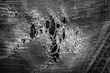 Close-up black and white texture photo of torn and damaged denim jeans cloth.