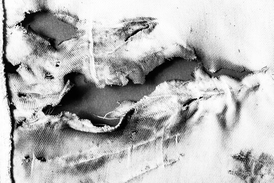 Close-up black and white texture photo of torn, burned and damaged cloth.