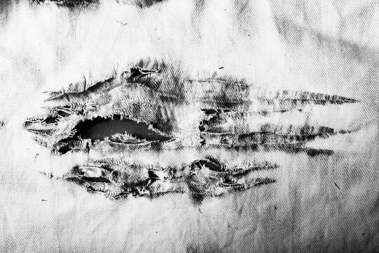 Close-up black and white texture photo of torn, burned and damaged cloth.