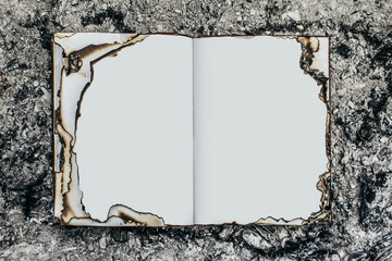 Close-up photo of opened book with burned pages laying on ashes surface.