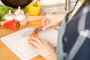 Obraz na płótnie Canvas Asian young woman, girl or housewife hand using knife, cutting carrots on board, on wooden table in kitchen home, preparing ingredient, recipe fresh vegetables for cooking meal. Healthy food people.