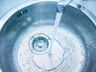 A stream of clean water drink flows from the kitchen faucet into the stainless steel sink. Environment, water pollution and water shortage concept