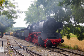 Fototapeta na wymiar Black and red antique steam train in the tracks with some smoke.
