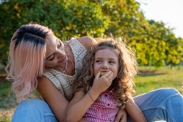 Fototapeta premium Mother and daughter together in a park on a picnic, daughter having a snack