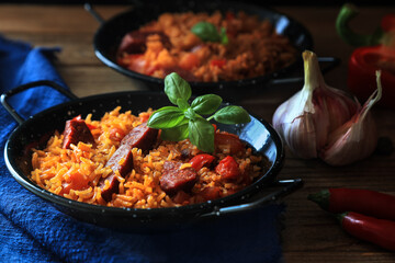 Spanish food specialty - chorizo sausage cooked with rice, tomatio, paprika, onion, garlic and saasoned with smoked paprika powder - basil leaf decoration on top (dark and moody photography)