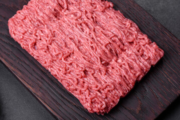 Fresh minced beef on cutting board on dark background with ingredients for cooking