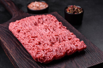 Fresh minced beef on cutting board on dark background with ingredients for cooking