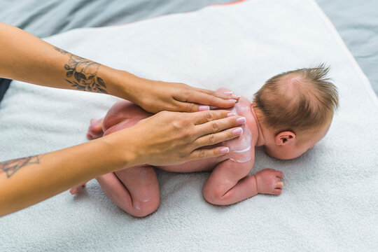 Cosmetics and skincare for babies. Caucasian infant baby boy lying on his belly and being massaged with delicate baby lotion by his tattooed mother. High quality photo