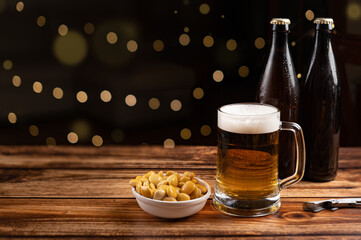 Beer served from a brown bottle into a long glass and a bowl of salted lupins on an wooden bar table with bokeh lights. Copy space