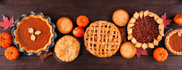 Assorted homemade fall pies. Pumpkin, apple and pecan. Top view table scene on a dark wood banner background. - obrazy, fototapety, plakaty
