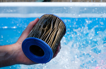 Dirty Replacement Pool Filter Cartridge in a man's hand on water splash background. Pool water...