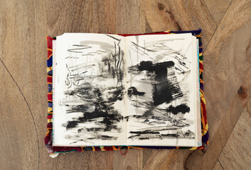 Abstract and expressive art. Top view of an artist's notebook with modern non figurative black and white drawings on the wooden table.