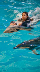 Vertical picture of a woman riding a dolphin swims in the pool.