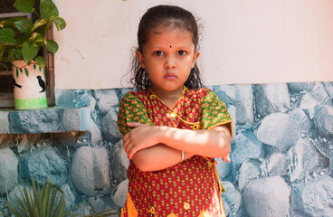 angry Indian young girl in traditional cloth looking at the camera with folded arms or hand.  selective focus on subject and background blur. 