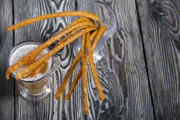 Thin sausages for beer in a beer glass. Next to it is a glass of wheat beer. Background from pine boards. Close-up.
