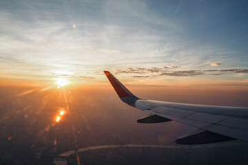 The wings of a passenger plane flying over Bangkok in the morning sun.