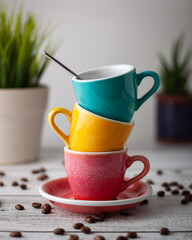 Three coffee cups of different colors stacked, with coffee beans in the table