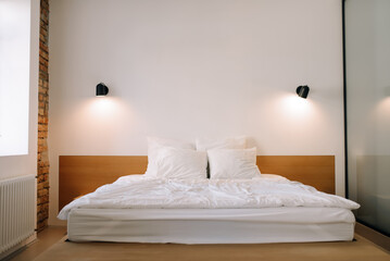 Stylish bright bedroom with wooden bed and white bed linen in apartment