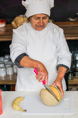 Mexican chef preparing breakfast using a knife to cut a melon. 
