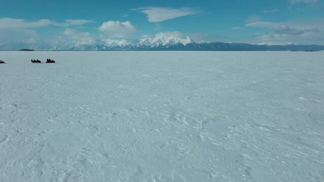 cinematic aerial view of cortege of snowmobiles riding in arctic endless landscape on the background of blue sky and mountains on the horizon