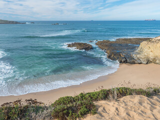 View of empty Praia do Sissal sand beach with ocean waves and sharp rock and cllifs at wild Rota Vicentina coast near Porto Covo, Portugal.