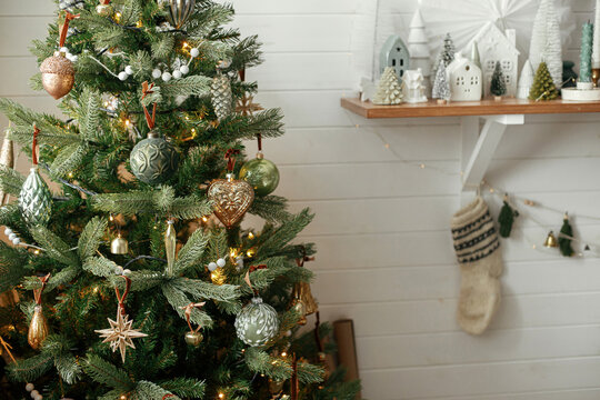 Christmas Tree With Vintage Baubles And Little Christmas Village Decoration. Modern Christmas Tree And Stylish Little Trees And Houses Scene In Festive Decorated Room. Atmospheric Winter Holidays