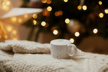 Warm cup of coffee on background of christmas tree with lights. Cozy home. Atmospheric winter...