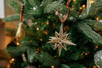 Christmas tree with vintage star and baubles with golden lights close up. Modern decorated christmas tree branches with stylish ornaments in festive room. Winter holidays, atmospheric time