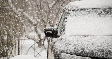 Snowfall paralyzed traffic, covering cars and roads with snow. Door mirror and glass of a car in the snow. Road safety.