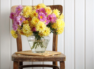 Pink and yellow chrysanthemums, autumn garden flowers in a glass vase on a chair.