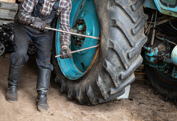 Change agricultural tractor broken tube tire at home. Man worker use crowbars to pry beneath the...