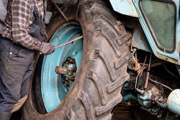 Change agricultural tractor broken tube tire at home. Man worker use crowbars to pry beneath the...