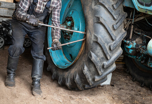 Change agricultural tractor broken tube tire at home. Man worker use crowbars to pry beneath the edge of the rim and break the bead. 