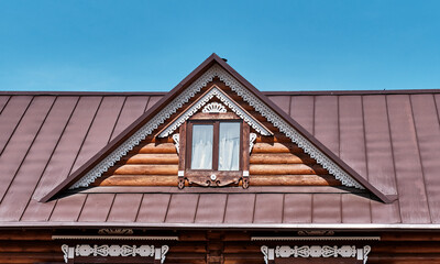 Facade of dormer window on roof of rural house in Buryatia. Carved wooden architraves.