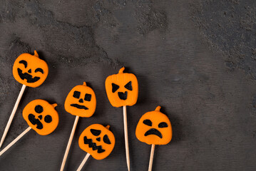 Halloween holiday. Creamy jelly candies in the shape of a pumpkin, on a wooden stick. Dark background. Top view. Copy space