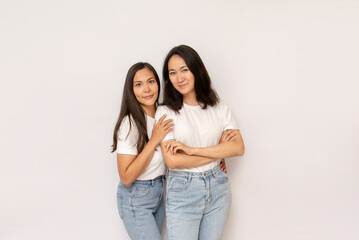 2 attractive brunette sisters or girlfriends on white background copy space. happy young asian women in white t-shirts