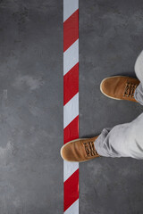 Man step over barrier tape and old boots shoes at cement floor background. Signal warning tape