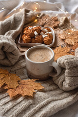 Obraz na płótnie Canvas Cozy autumn still life: a warm sweater, autumn leaves, lights, a mug of cappuccino and a plate of cookies. Concept for wishing a good autumn morning. Selective focus.
