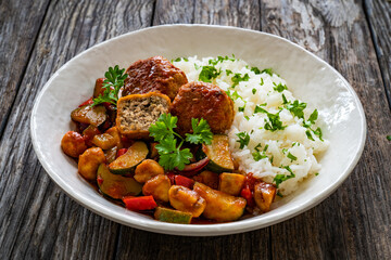 Delicious stew - white rice with vegetables and meatballs on wooden table

