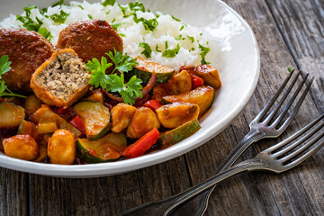 Delicious stew - white rice with vegetables and meatballs on wooden table
