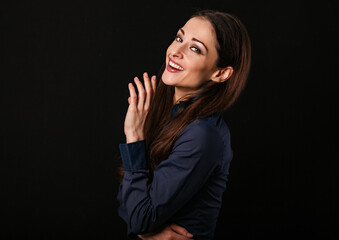 Beautiful thinking toothy laughing business woman with hand near the face in blue shirt on black background with empty copy space for text. Closeup