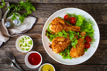 Panko crusted baked chicken drumsticks with greens on wooden table
