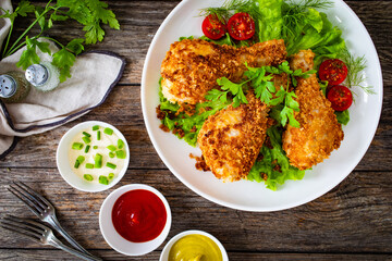 Panko crusted baked chicken drumsticks with greens on wooden table
