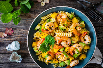 Fusilli with prawns, mango, avocado and mint on wooden table
