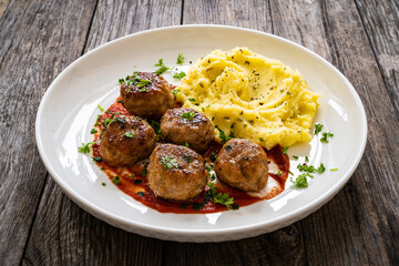 Fried pork meatballs with potato puree and tomato sauce on wooden table
